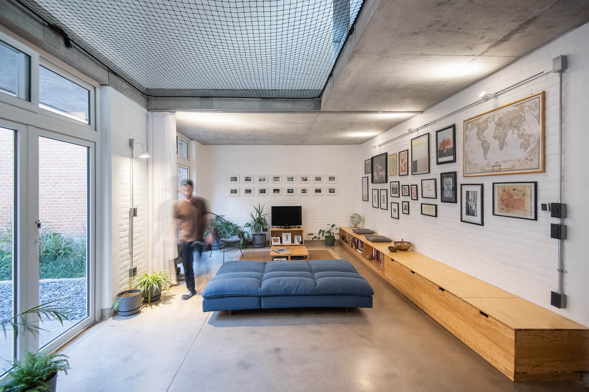 Diseño de sala de estar por fábrica de espacios con muebles en madera clara con estilo industrial muros de ladrillo blanco con retratos