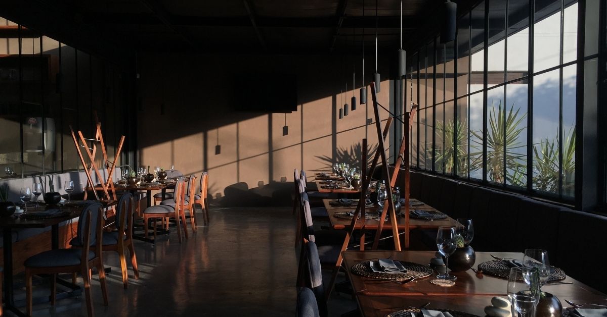 Mesas en interior de restaurante Xoconostle, acabados de diseño de madera y ladrillo lamparas colgantes circulares iluminando el espacio diseño de iluminación por Lucas Salas.