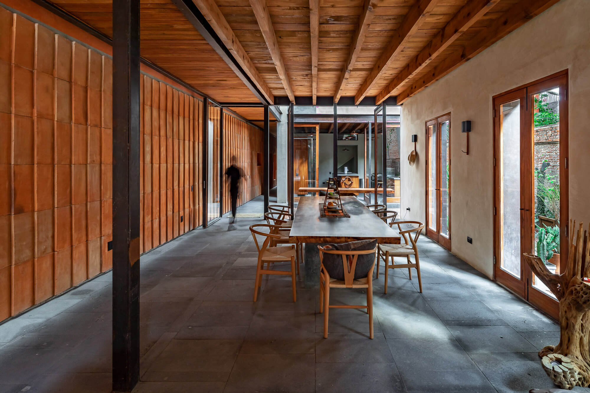 Persona caminando dentro de comedor con muros de ladrillo, techo y muebles de madera con acabado rústico moderno