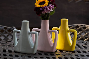 Floreros de diferentes colores posando en una mesa de metal con dos sillas al fondo